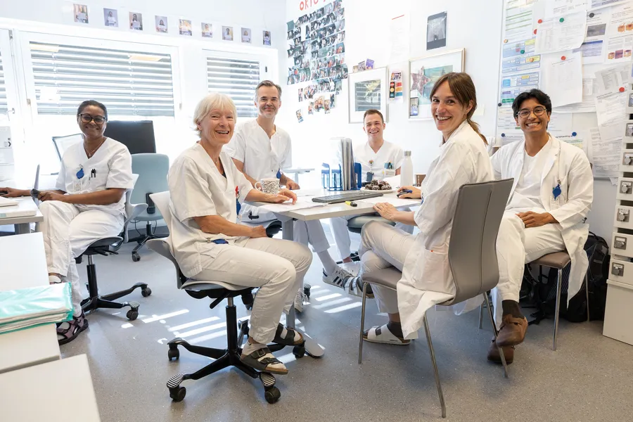 En gruppe mennesker i hvite labfrakker sitter ved et bord