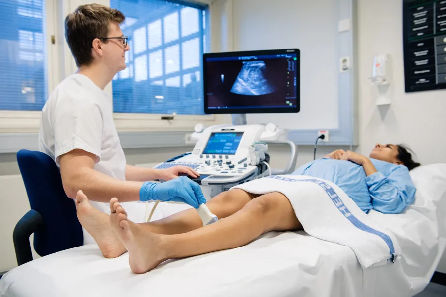 Mannlig radiolog foretar ultralydundersølkelse på  leggen til kvinne i seng