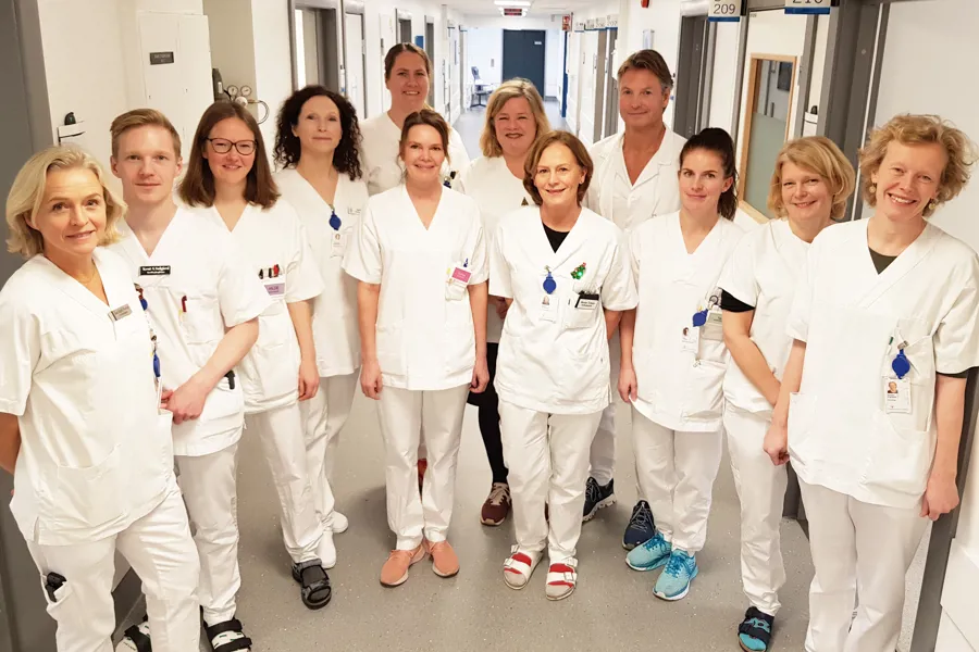 12 hvitkledde ansatte på Kreftsenteret står på rad og rekke i korridoren og smiler til fotografen