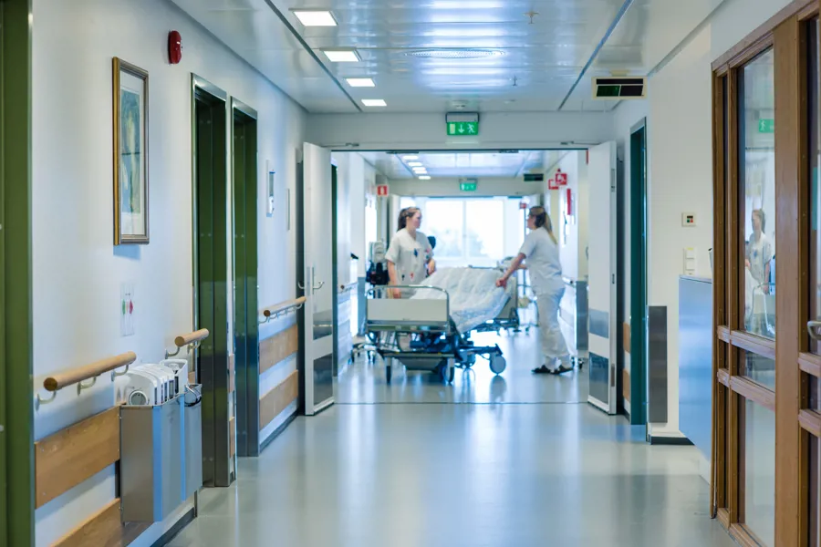 Korridor med sykepleiere som triller en pasient i seng