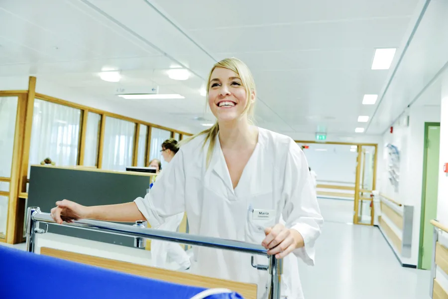 Smilende sykepleier triller en sykehusseng