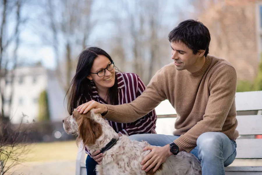 En mann og kvinne som sitter på en benk med en hund