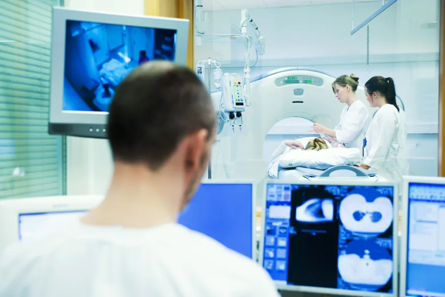 Radiologist looking at screen. Two nurses and MR-machine in the background